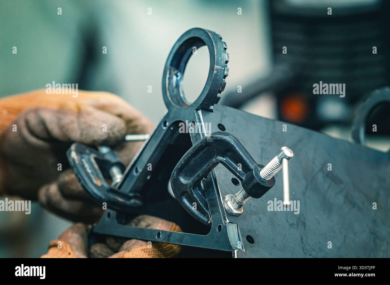 Mit den männlichen Händen werden Metallteile mit einer Schelle festgezogen. Die Schelle verfügt über eine Gewindeschraube zum Festziehen und Einstellen des Drucks. Hintergrund der Industriewerkstatt. Stockfoto