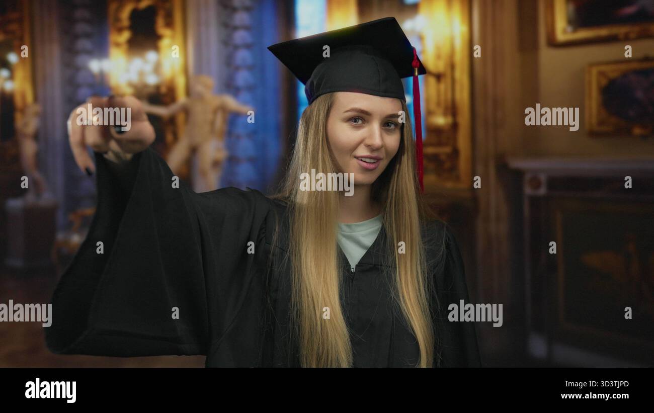Die junge Frau im Abschlusskleid posiert selbstbewusst in einem eleganten Museum, das Kunst- und Kulturhighlights zeigt. Stockfoto