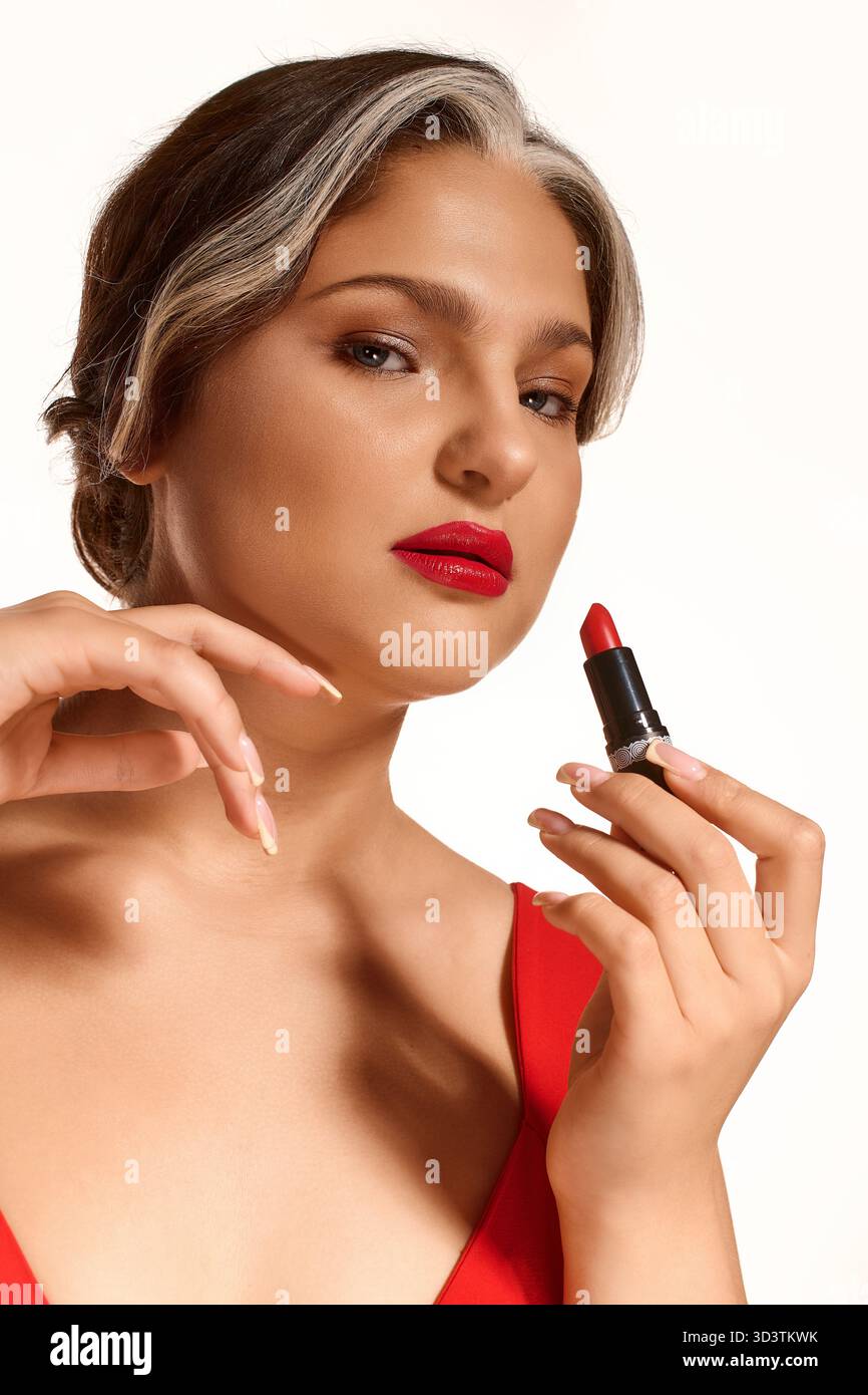 Eine junge Frau trägt roten Lippenstift auf, der ihre auffälligen Merkmale und die weiße Stirnpartie betont. Stockfoto