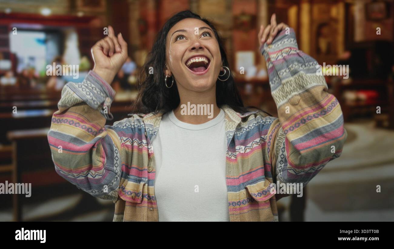 Frau, die mit dem Finger nach oben zeigt, mit lächelndem Gesicht und erhobener Hand in einem katholischen Kircheninnenraum zwischen Holzbänken; Freude an Danksagung. Stockfoto