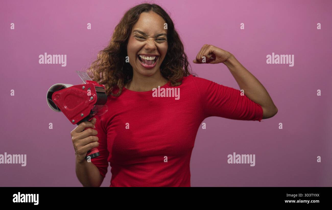 Frau mit Klebebandspender und flexiblem Bizeps im Studio mit rosa Hintergrund und breitem lachenden Lächeln; Selbstvertrauen-Feier. Stockfoto
