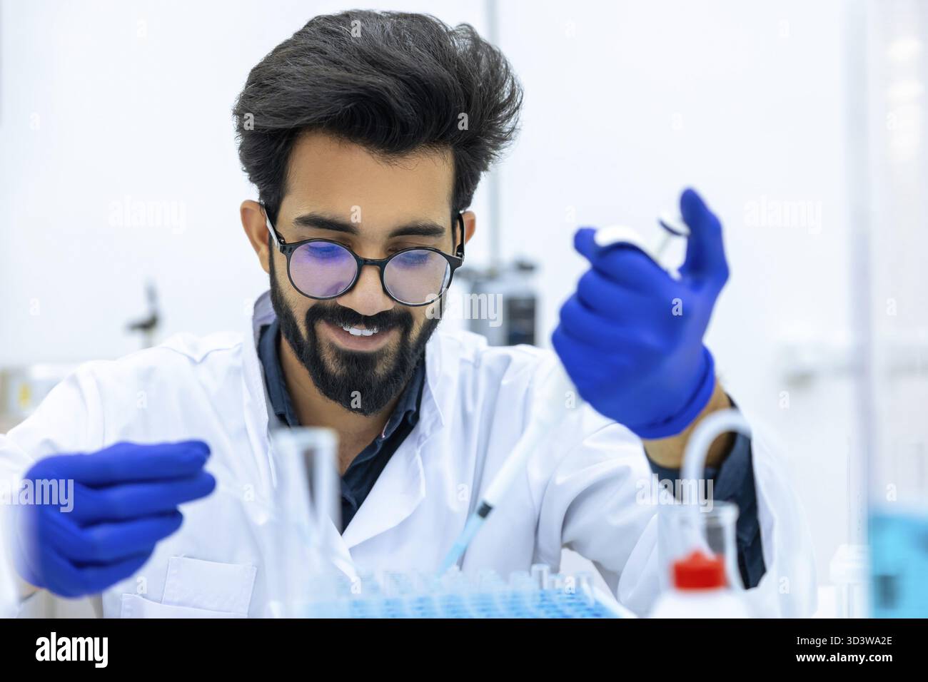 Mann Wissenschaftler mit Schutzhandschuhen Tropfen Chemikalien in Reagenzgläser, Biochemiker führt Experimente durch, um neue Medikamente zu entdecken, arbeitet in der Wissenschaft Stockfoto