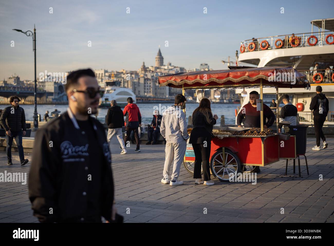 Geröstete Kastanienverkäufer am Ufer des Goldenen Horns mit Galatenturm in der Ferne - Istanbul, Türkei. Stockfoto