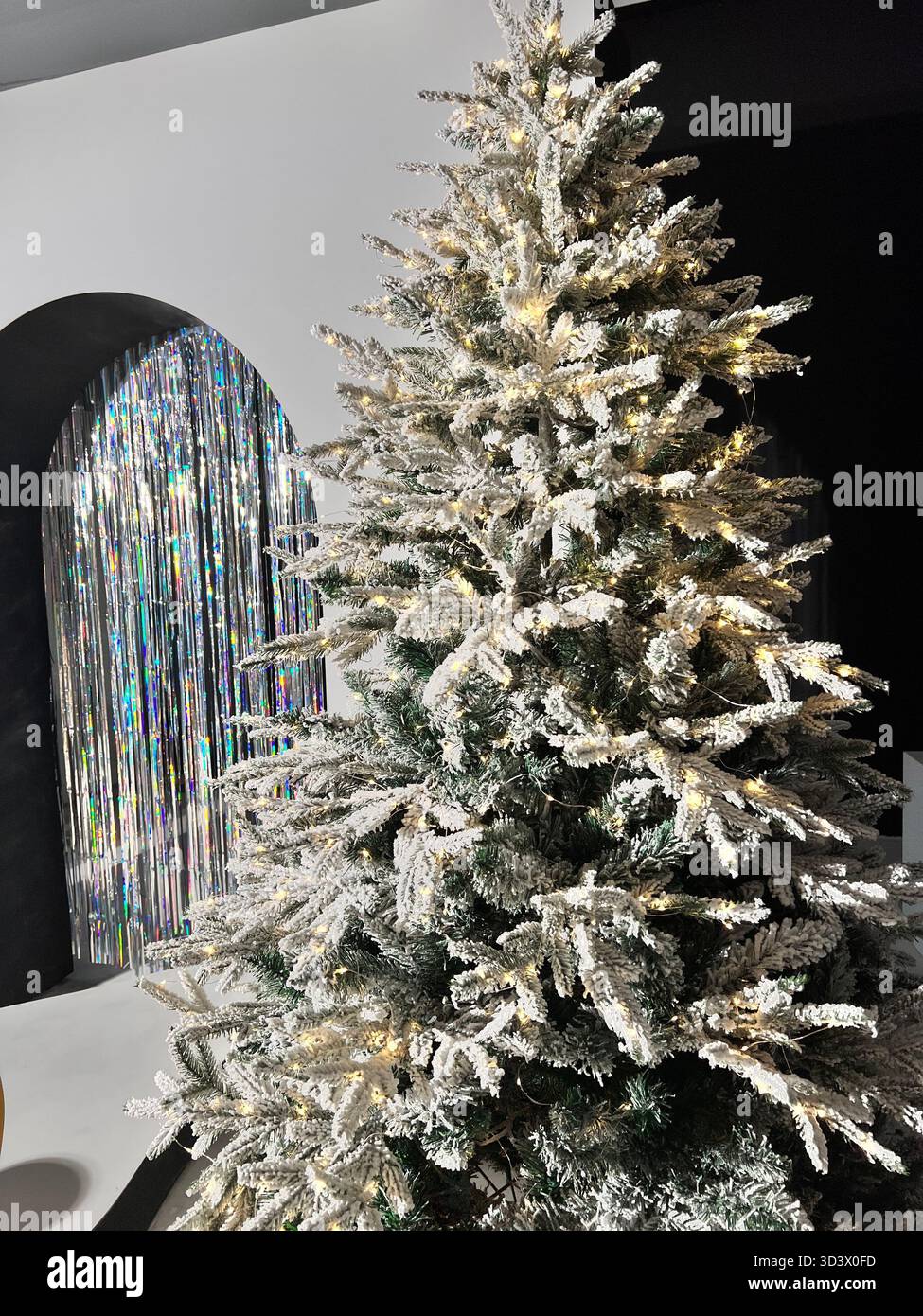 Künstlicher Weihnachtsbaum im Schnee mit gelben Lichtern - Smartphone-aufgenommenes Stockfoto