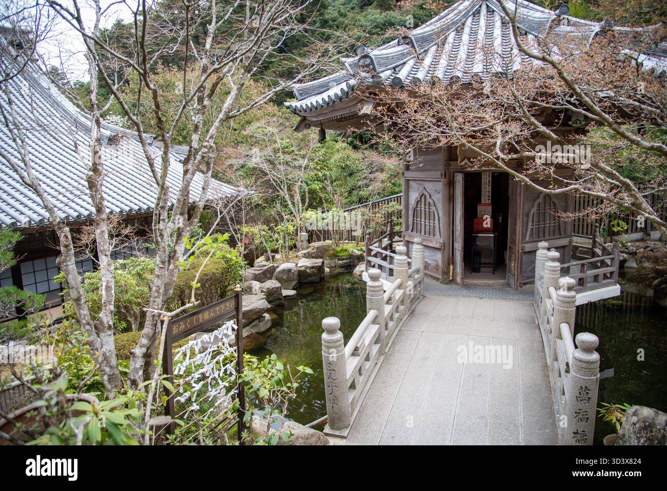 Ein kleiner hölzerner Tempelpavillon, umgeben von Bäumen und einem Koi-Teich, der traditionelle japanische Gartenästhetik und buddhistische Harmonie mit der Natur widerspiegelt. Stockfoto