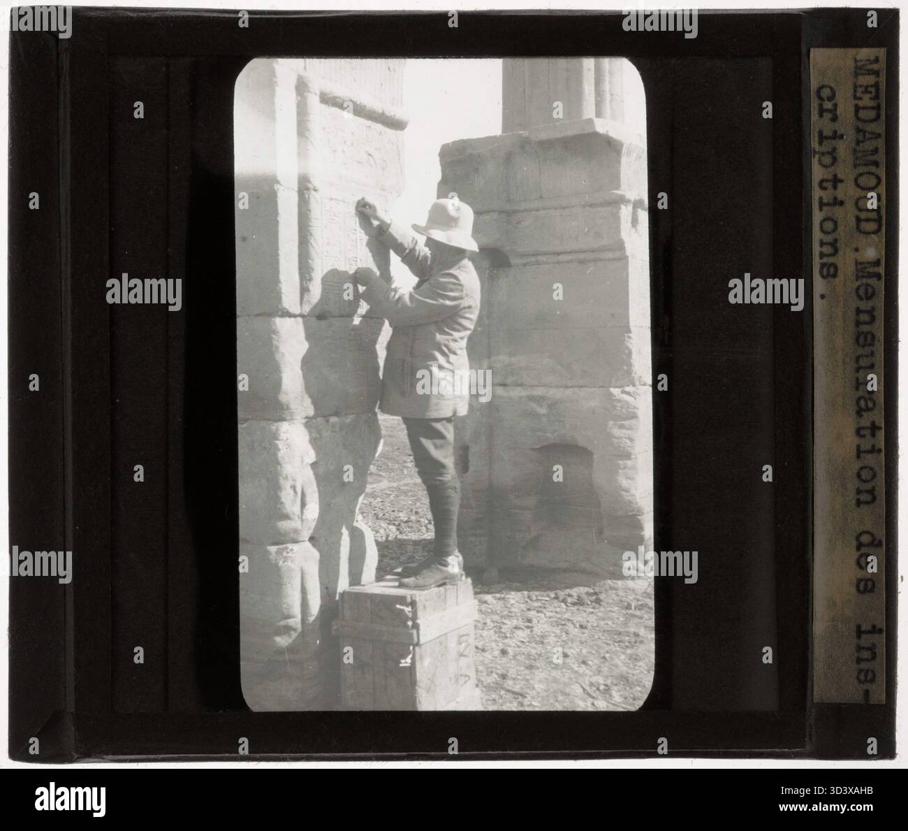Dieses Glasdiapositiv aus der Zeit um 1924-1932 zeigt Fernand Bisson de la Roque, einen französischen Archäologen, der Inschriften auf dem Stein im Tempel von Montu in Medamud misst. Seine Arbeit trug zur Dokumentation und Untersuchung ägyptischer Hieroglyphen bei. Stockfoto