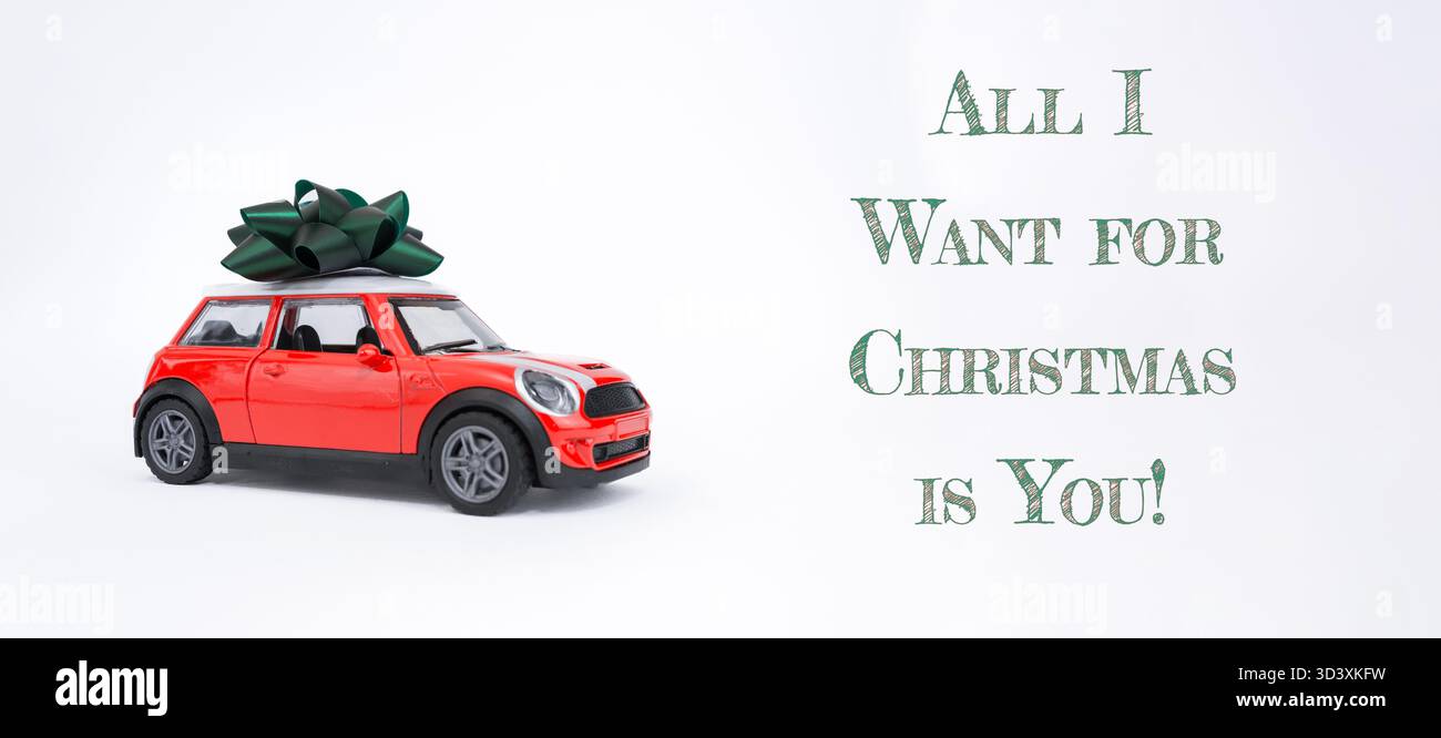 Ein leuchtend rotes Spielzeugauto mit grünem Bogen repräsentiert die Freude an Weihnachtsgeschenken und festlichen Feierlichkeiten und weckt Feiertagsstimmung und Spannung Stockfoto