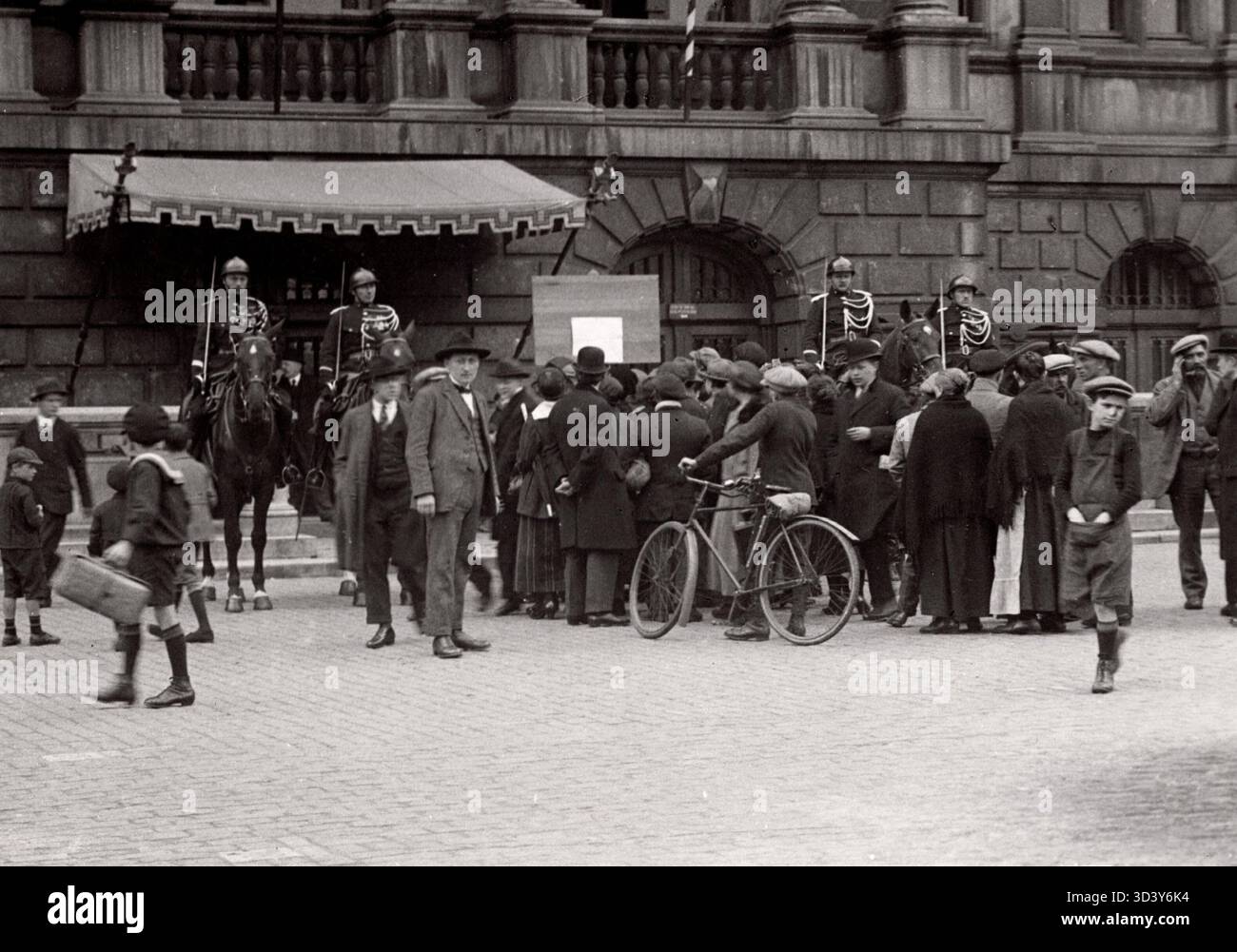1923 versammeln sich eine Gruppe von Zuschauern vor einem Gebäude mit Baldachin und vier Militärreitern, um eine Ankündigung über die Einführung des Prangers in Belgien zu lesen. Stockfoto