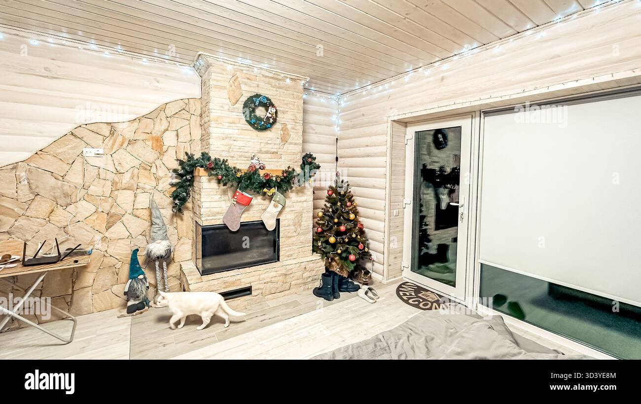Das warme und einladende Wohnzimmer verfügt über einen wunderschön dekorierten Weihnachtsbaum, Strümpfe, die am Kamin hängen, und sanfte Beleuchtung, perfekt für holi Stockfoto