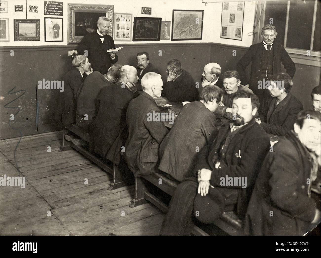 1911 hält ein Mann eine Bibelvorlesung und eine Rede nach dem Abendessen im Nachtlager „Meneertje“ in den Haag. Dieses Foto zeigt die Rolle religiöser Dienste in der Sozialhilfe während des frühen 20. Jahrhunderts. Stockfoto