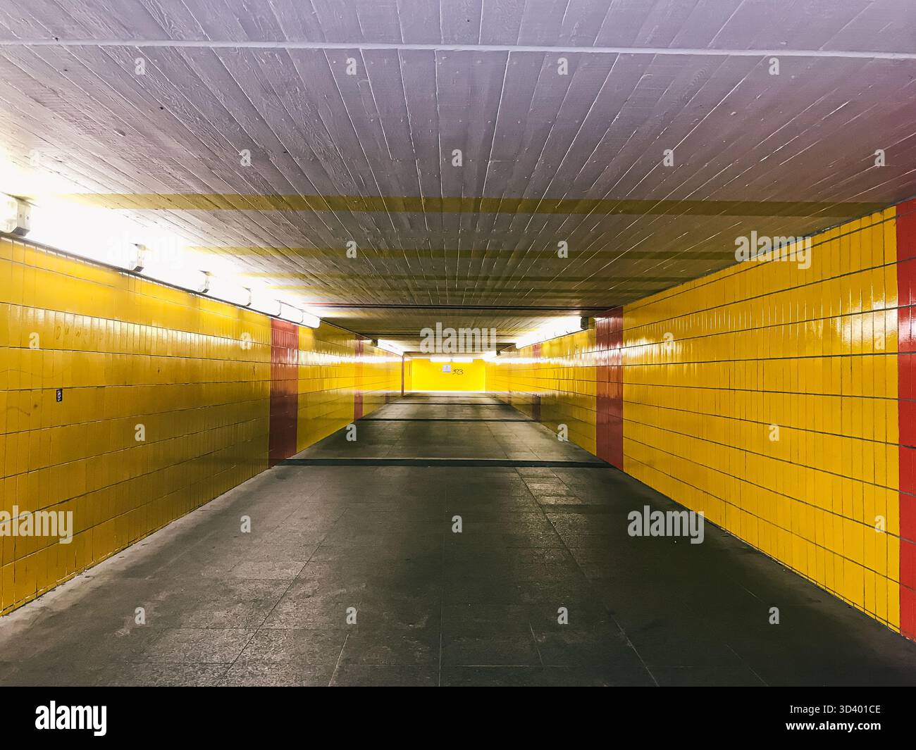 Der unterirdische Tunnel verfügt über leuchtend gelbe Fliesen, glatten Betonboden und helle Beleuchtung, die eine einladende Atmosphäre schaffen Stockfoto