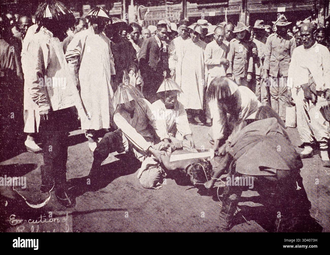 Dieses Foto von 1900 bis 1906 zeigt eine öffentliche Hinrichtung in Peking, China. Neun verurteilte Verbrecher werden in einer belebten Straße hingerichtet, wobei neugierige Zuschauer das Ereignis beobachten. Das Foto zeigt die brutale Natur der öffentlichen Justiz im China des frühen 20. Jahrhunderts. Stockfoto