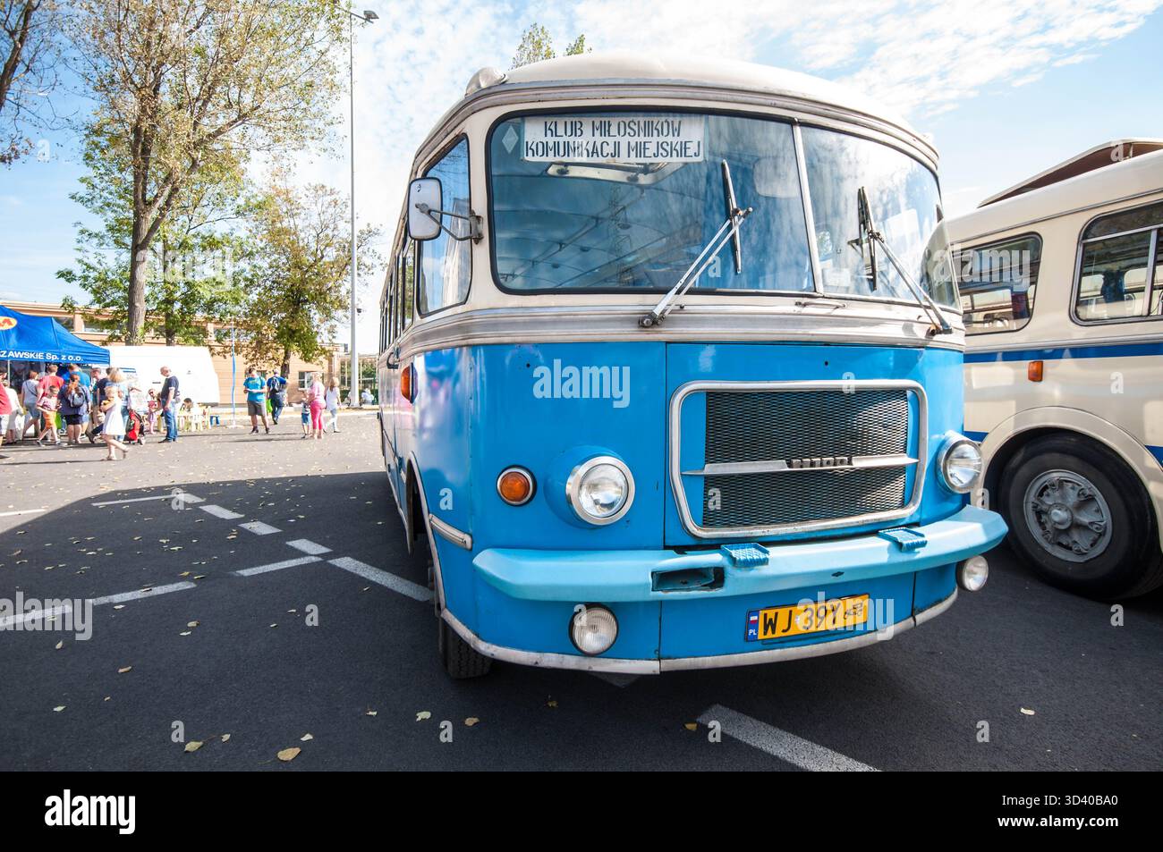 Ein blauer Vintage-Bus wird bei einer Veranstaltung mit öffentlichen Verkehrsmitteln im Freien gezeigt, bei der Menschen herumlaufen. Stockfoto
