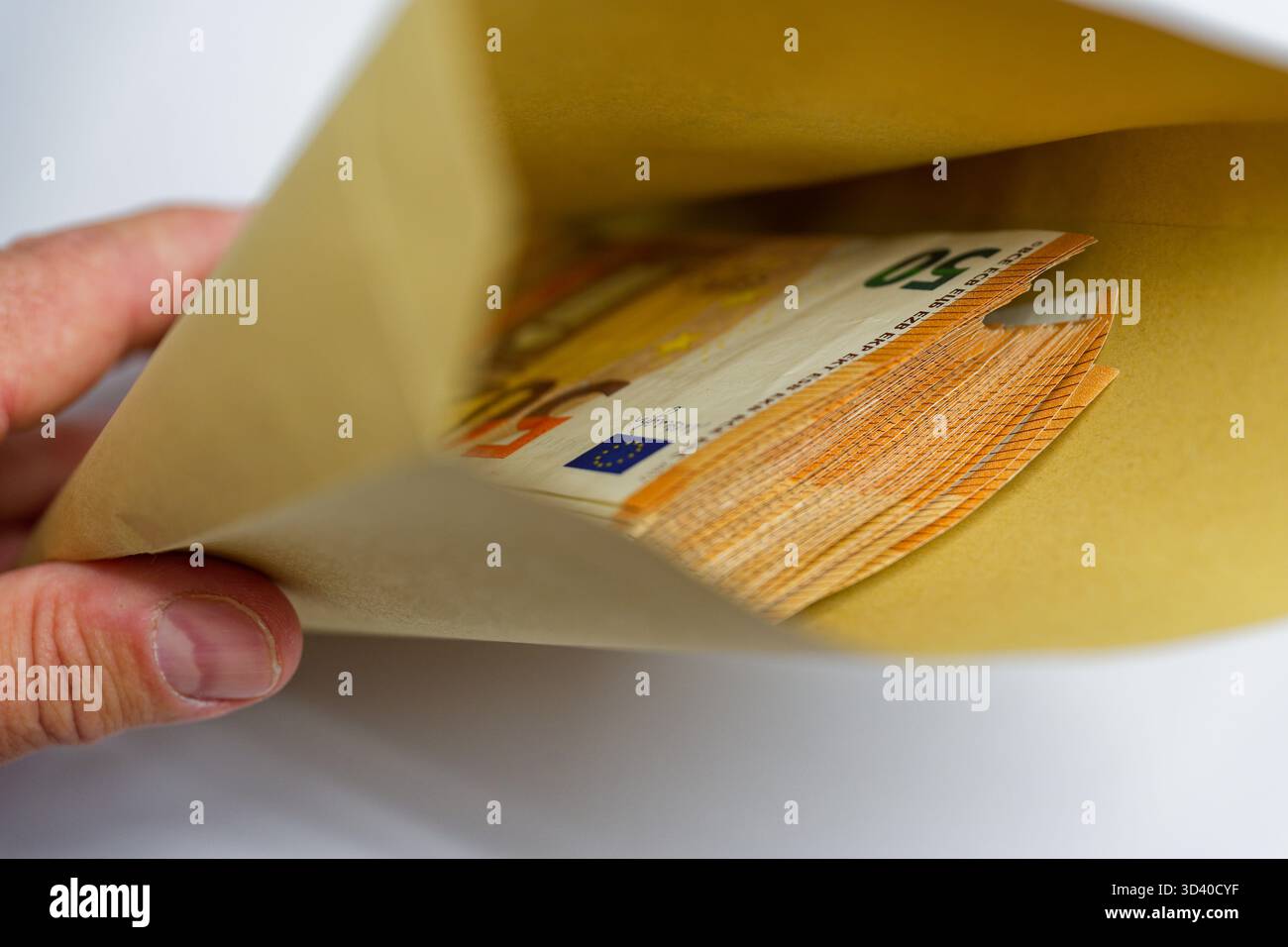 Eine Hand hebt einen gelben Umschlag an, während der Geldstapel herausblickt, die freiliegenden Kanten zeigen saubere 50-Euro-Banknoten und der Moment fühlt sich diskret an Stockfoto