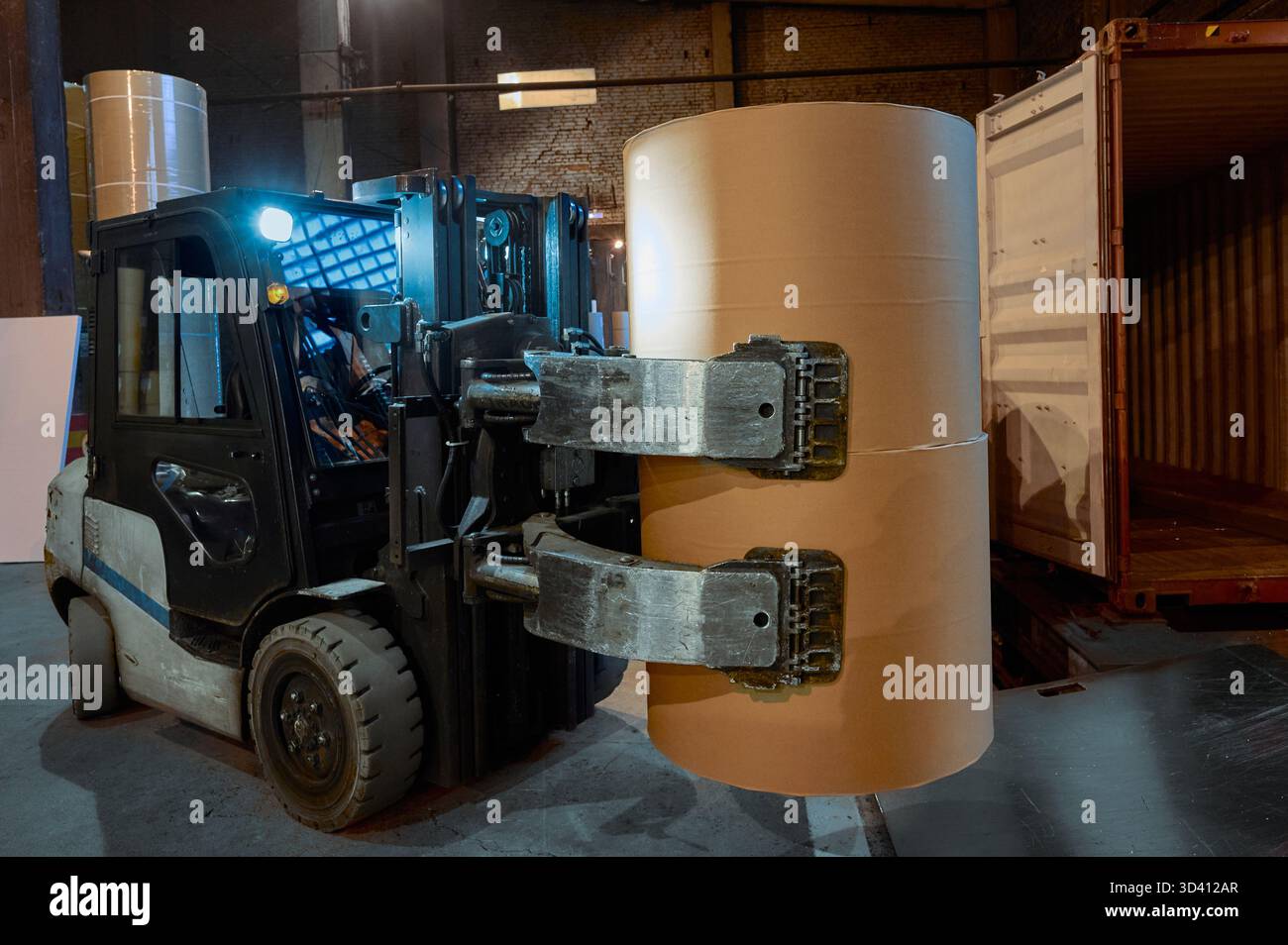 Große Gabelstapler, die Papierrollen in einem belebten Papierfabriklager während des Abendbetriebs handhaben Stockfoto