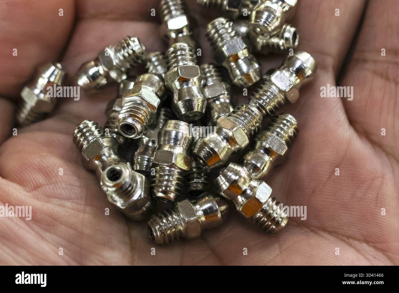 Nahaufnahme einer Handvoll neuer Nippelteile für Schmiernippel aus Metall für industrielle Schmierung und Wartung. Der Mitarbeiter hält glänzende Hardwarekomponenten im Stockfoto