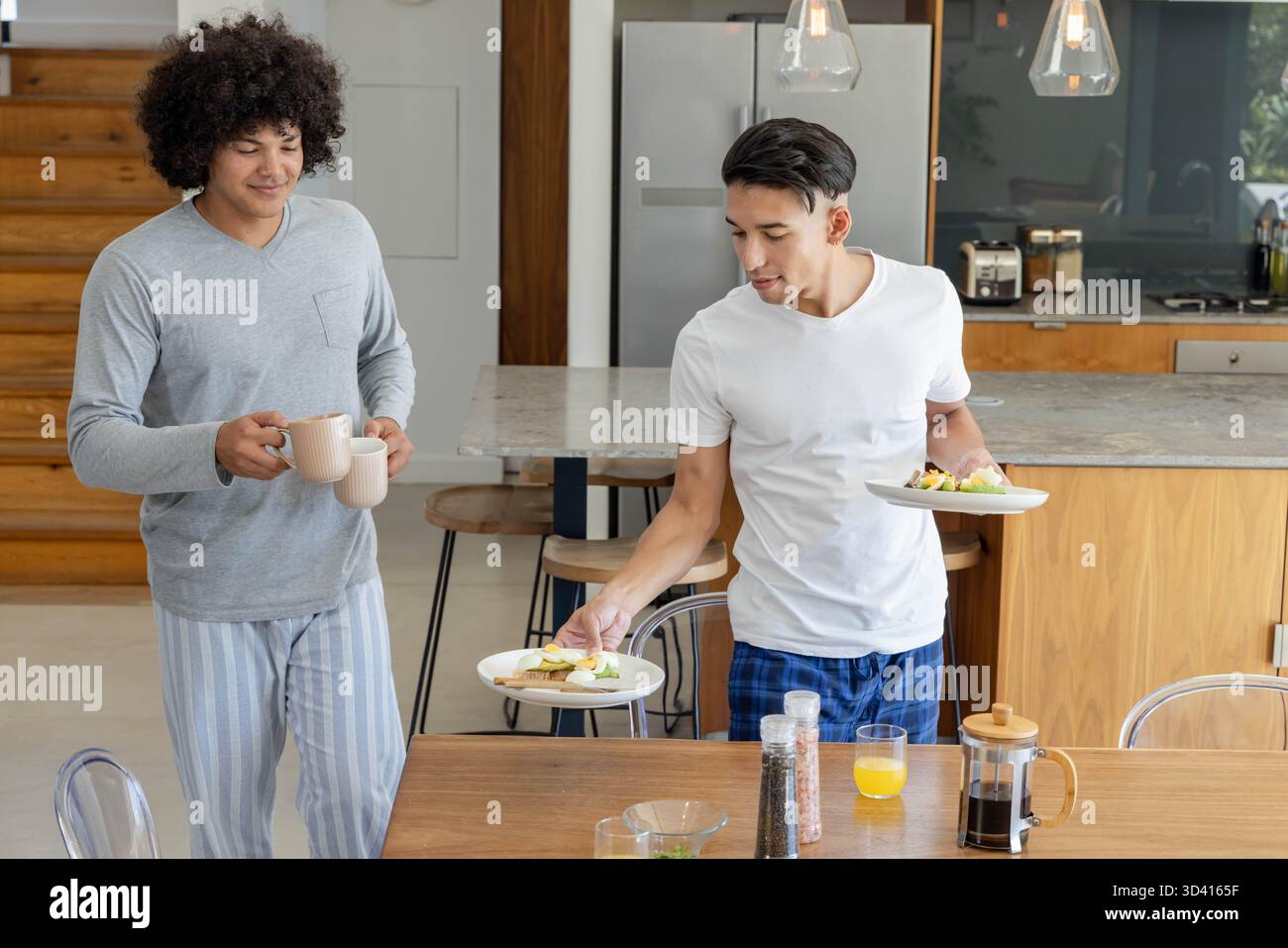 Mit Frühstücksplatten, verschiedenen männlichen Freunden, die zum Tisch in der Küche gehen, Kaffeemaschine Stockfoto