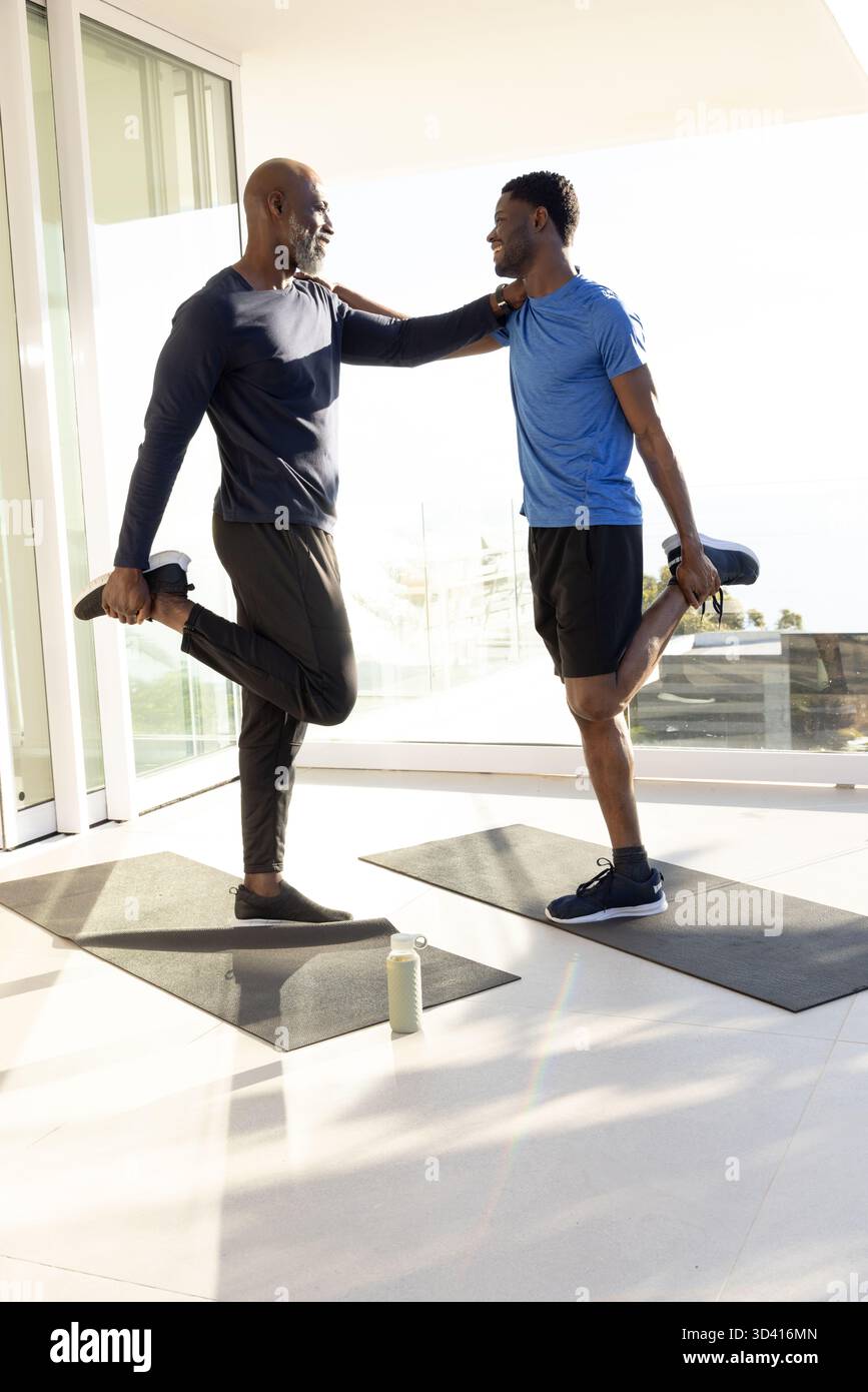 Afroamerikanische Freunde dehnen sich, während sie im Heimstudio auf einem Bein balancieren, mit Yogamatten Stockfoto