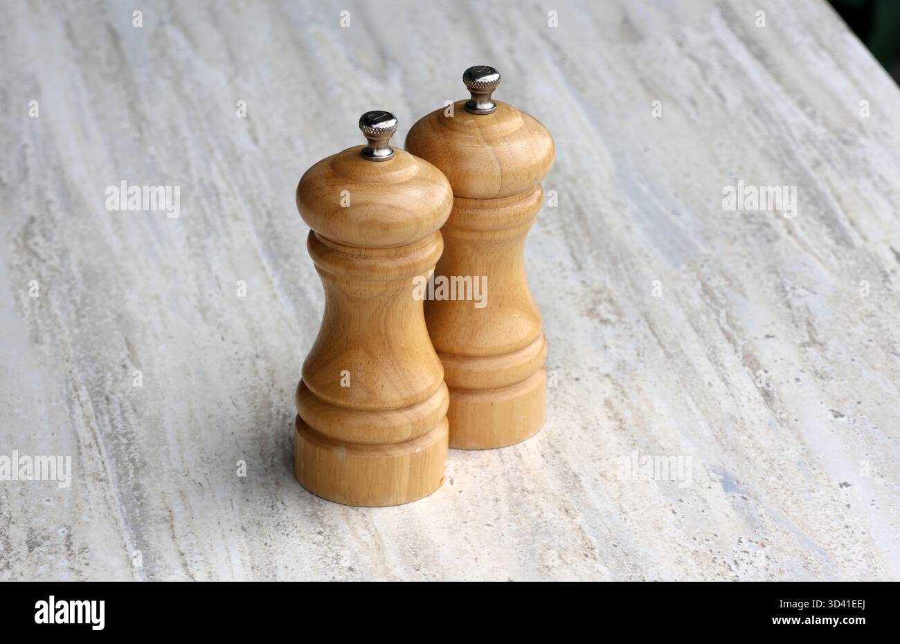 Zwei hölzerne Salz- und Pfeffermühlen sitzen nebeneinander auf einem hellen Tisch Stockfoto