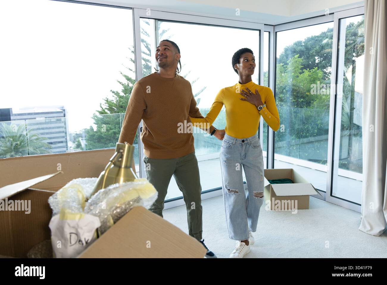 Verschiedene Paare packen Umzugskartons im Wohnzimmer des Apartments aus und erkunden den Raum mit Messinglampe Stockfoto