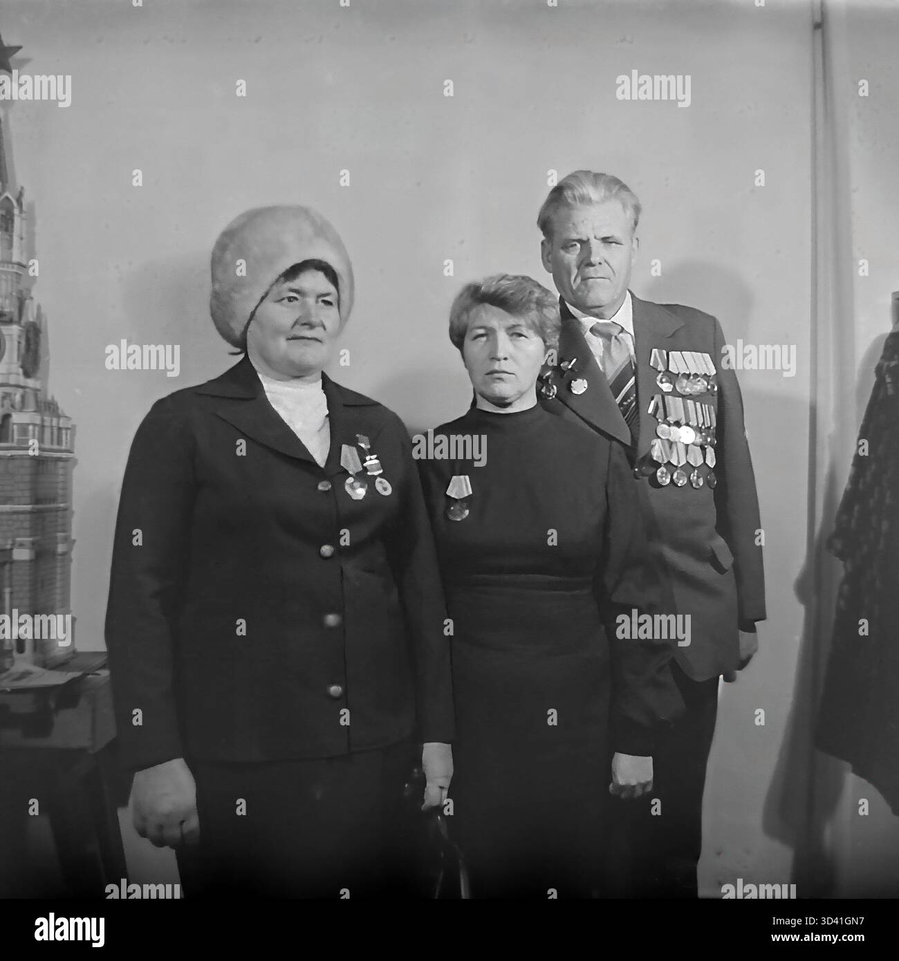 Ein Archivfoto aus dem Jahr 1984 zeigt Delegierte einer Stadtkonferenz im Kulturhaus Artyom in Sloviansk, Ukrainische SSR. Ein Gruppenporträt von drei Teilnehmern: Zwei Frauen und ein männlicher Veteran des Zweiten Weltkriegs. Alle drei sind mit sowjetischen Orden und Orden dekoriert. Die Frau links trägt einen großen Pelzhut, was auf kaltes Wetter hinweist. Sie stehen in der Nähe eines komplizierten Modells, möglicherweise des Kremls. Dies fängt die geehrten Teilnehmer einer offiziellen sowjetischen Veranstaltung ein. Dies zeigt den Alltag im friedlichen Donbass vor dem Krieg. Stockfoto