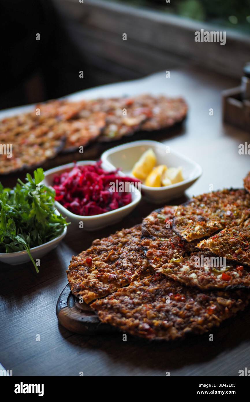 Nahaufnahme des traditionellen türkischen lahmacun, serviert mit Petersilie, Zitrone und Salat auf einem Holztisch in einem lokalen Restaurant. Stockfoto