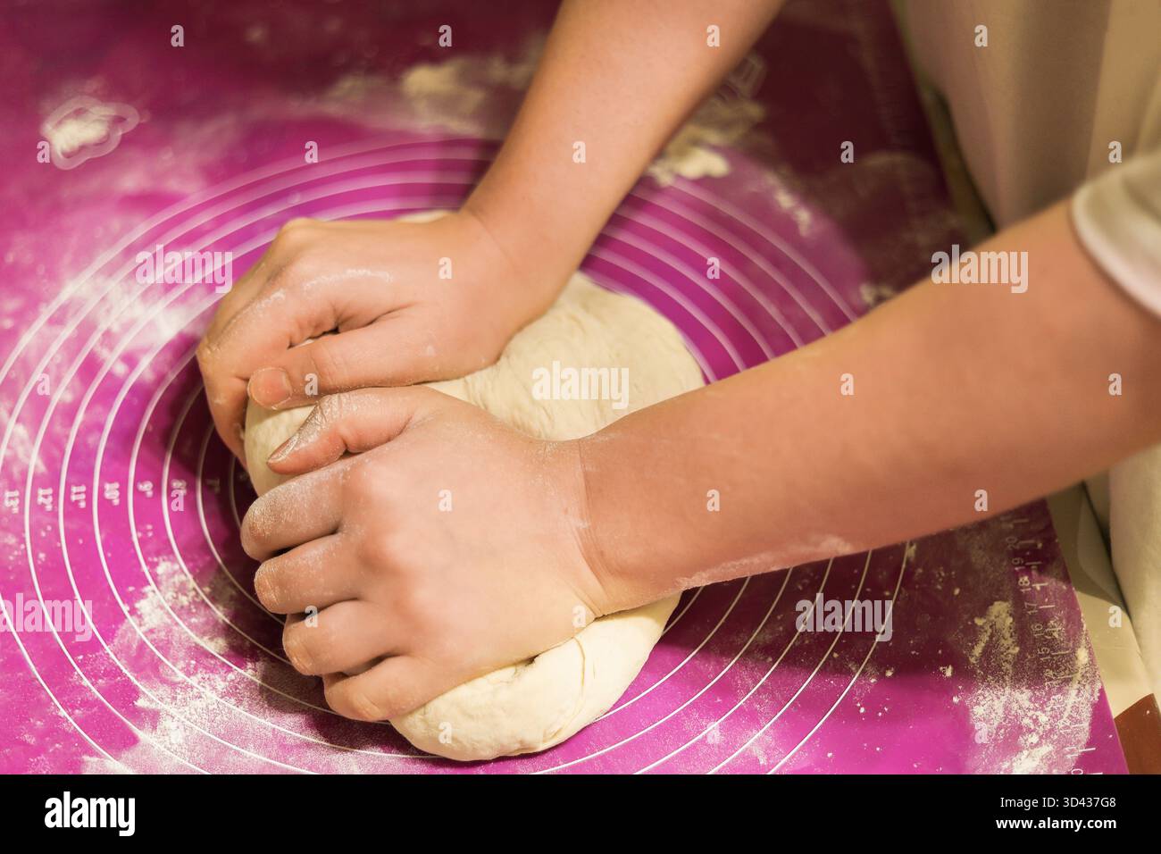 Eine Hand streut Mehl auf einen Hügel frischen Teigs, der auf einer violetten Silikon-Backmatte verknetet wird. Hochwertige Fotos Stockfoto