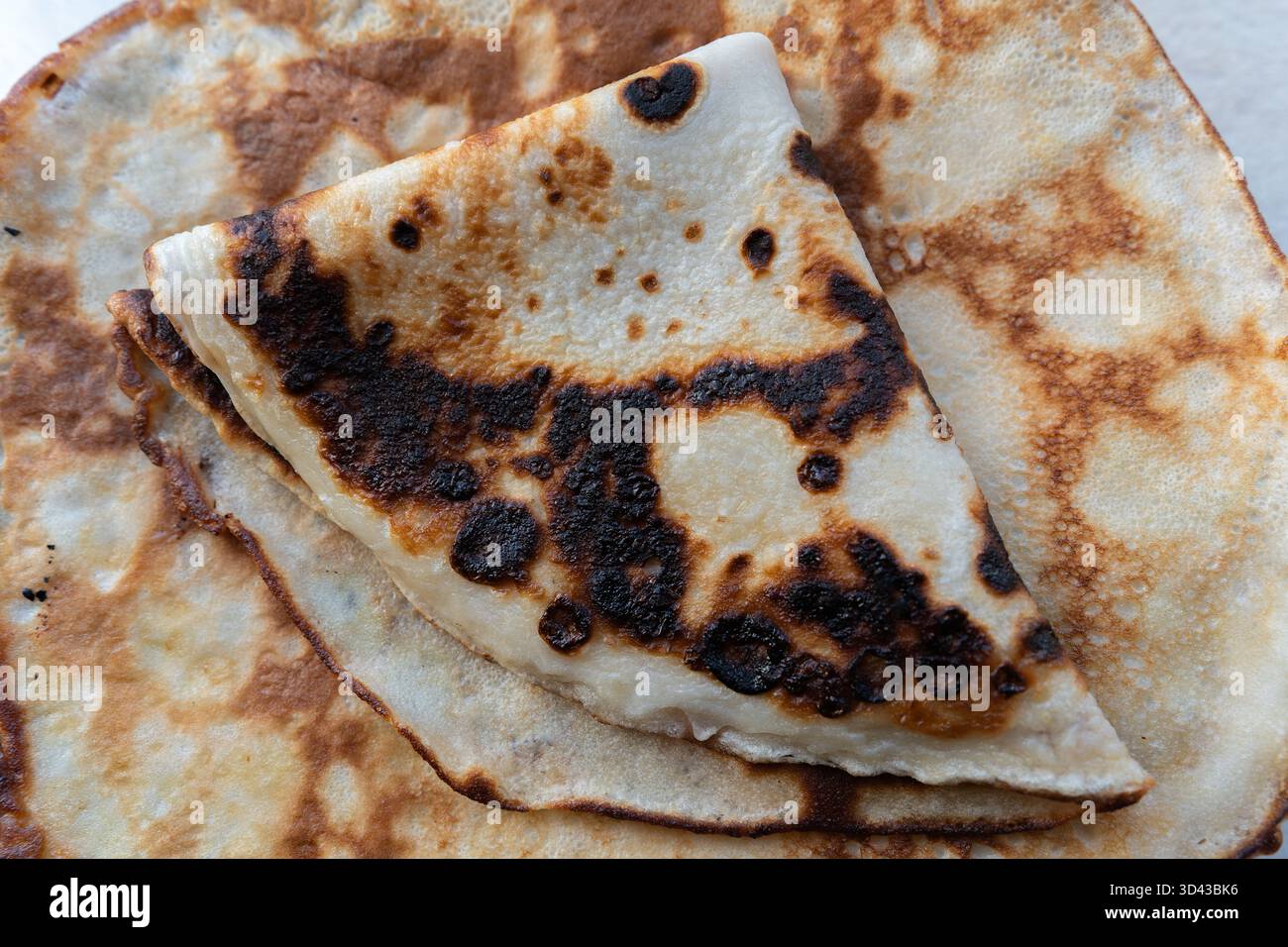 Detaillierte Makroaufnahme der unebenen Oberfläche eines Pfannkuchens mit goldbraunen und leicht gebrannten Mustern. Symbolisiert Komfortgerichte, Hausmannskost und Stockfoto