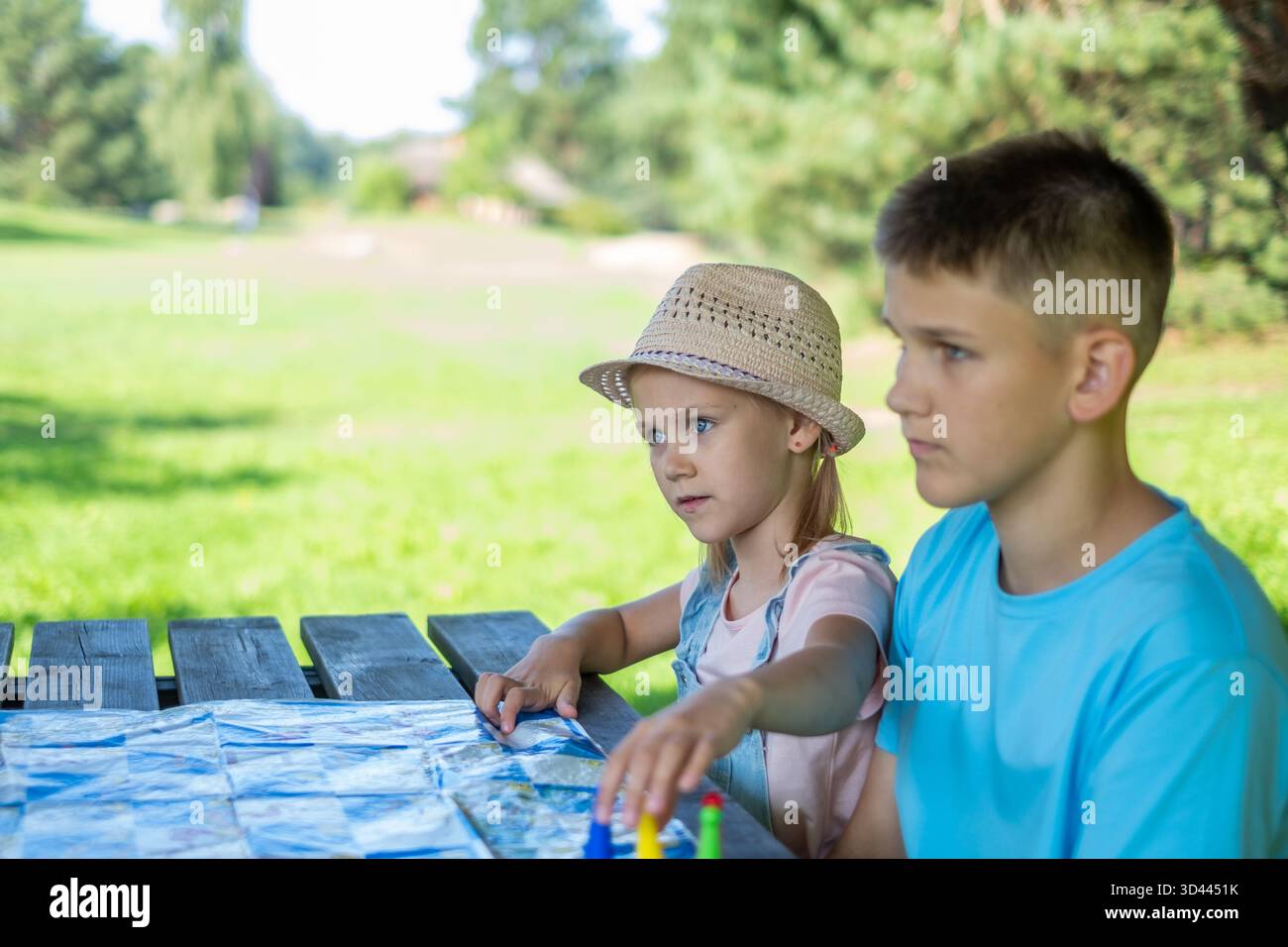 Kinder spielen im Freien ein Tischspiel in einem Park, demonstrieren Konzentration und Verbundenheit, mit grünem Gras und Bäumen, die eine ruhige Atmosphäre schaffen Stockfoto