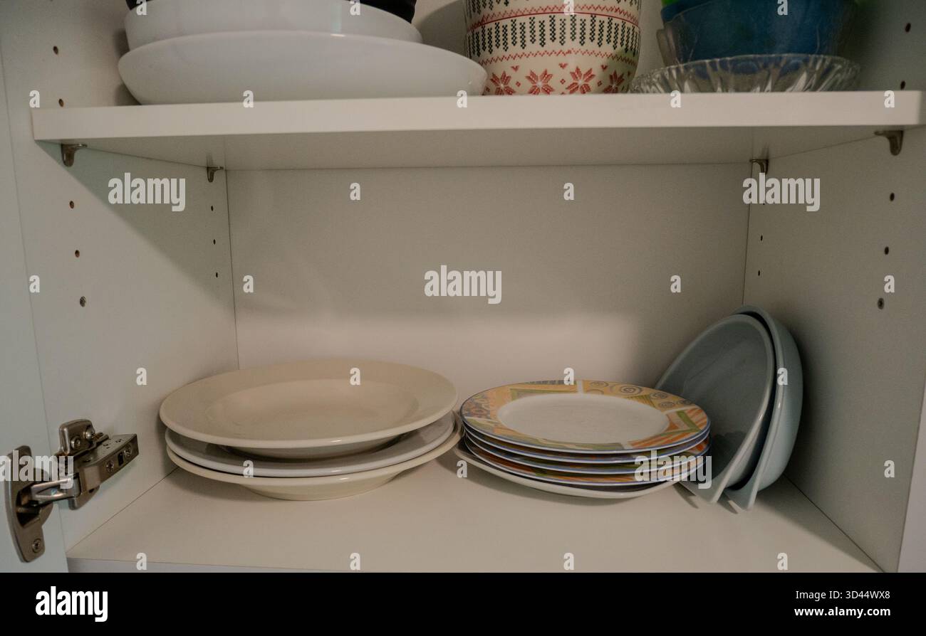 Stapelbare Keramikplatten und -Schüsseln in einem weißen Küchenschrank. Die klare Zusammensetzung betont die Organisation, Aufbewahrung und Minimalismus im Haushalt Stockfoto