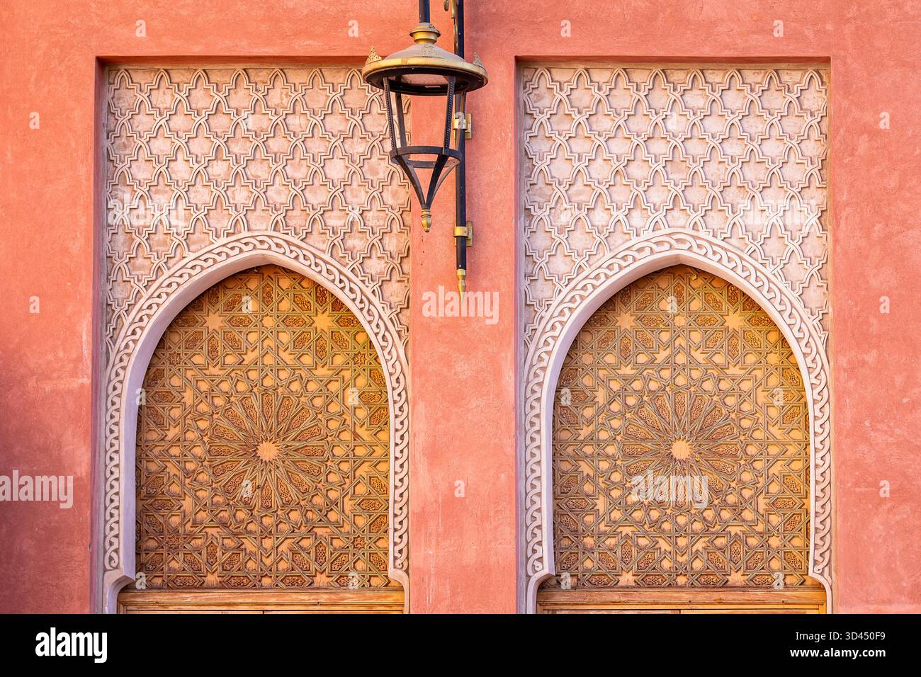 Marokkanische Architektur in Marrakesch Medina mit geschnitzten Bogentüren, geometrischen islamischen Mustern und einer Laterne unter kunstvollen Holzdetails. Stockfoto