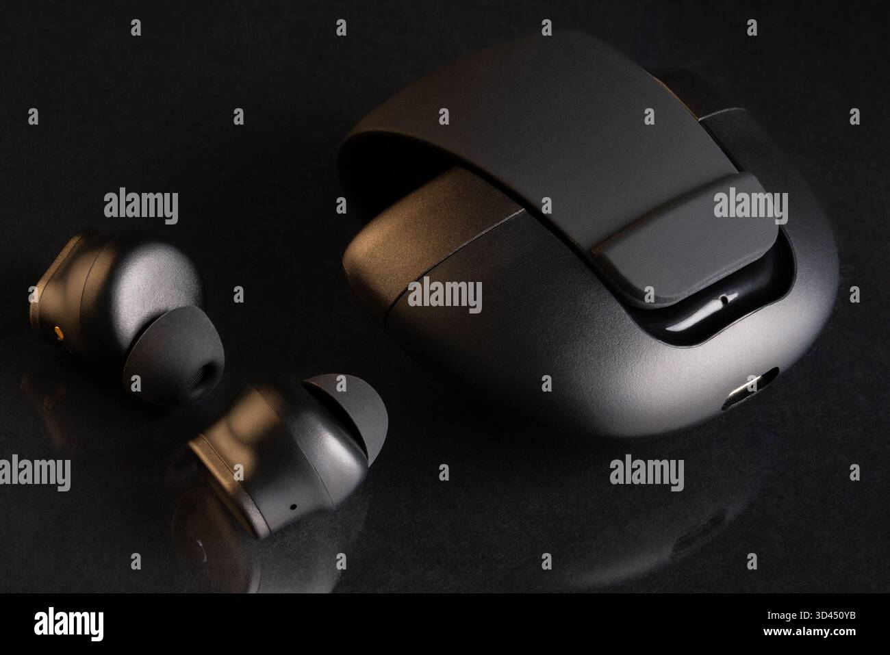 Nahaufnahme der eleganten schwarzen schnurlosen Ohrhörer und Ladetasche auf einem glänzend dunklen Hintergrund, die moderne Audiotechnologie zeigt. Stockfoto