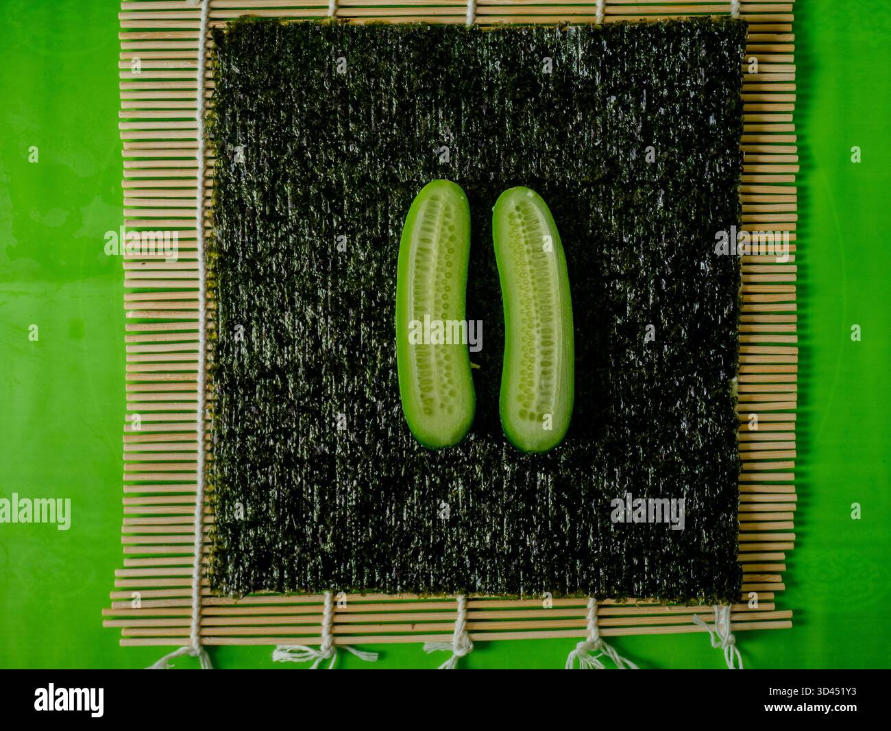 Draufsicht von zwei frischen Gurkenhälften auf Nori-Blatt und Bambusmatte, Zutat für Sushi-Zubereitung Foto für Küchen- und Kochkünstler. Hohe Qual Stockfoto