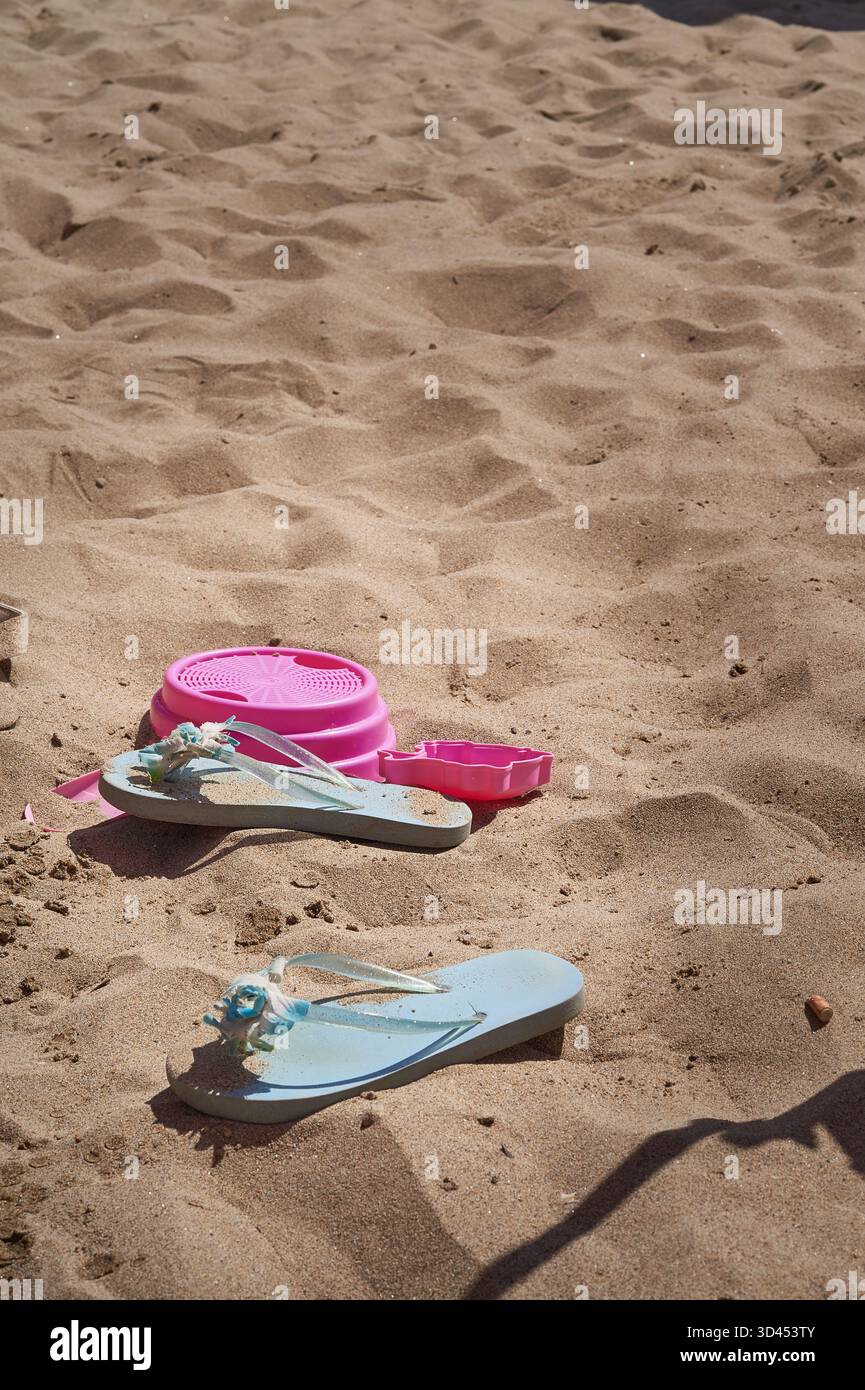 Blaue Pantoffeln und rotes Spielzeug auf dem Sand Stockfoto