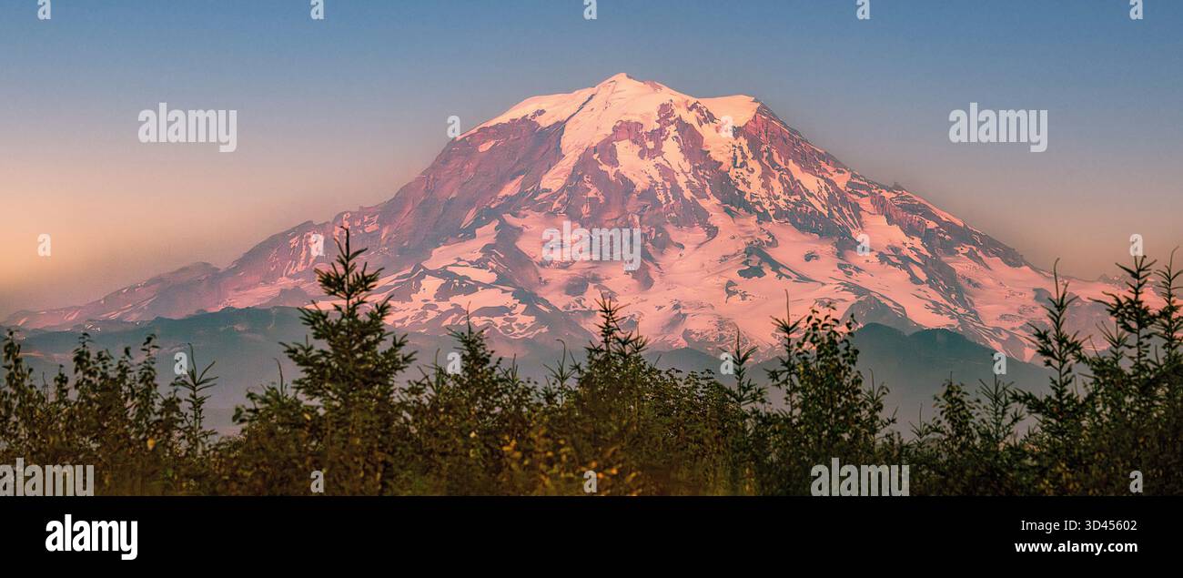 Sunset Mountain Majesty: Der Mount Rainier steht hoch im Mount Rainier National Park, dessen schneebedeckter Gipfel von der untergehenden Sonne beleuchtet wird. Die Berge Stockfoto