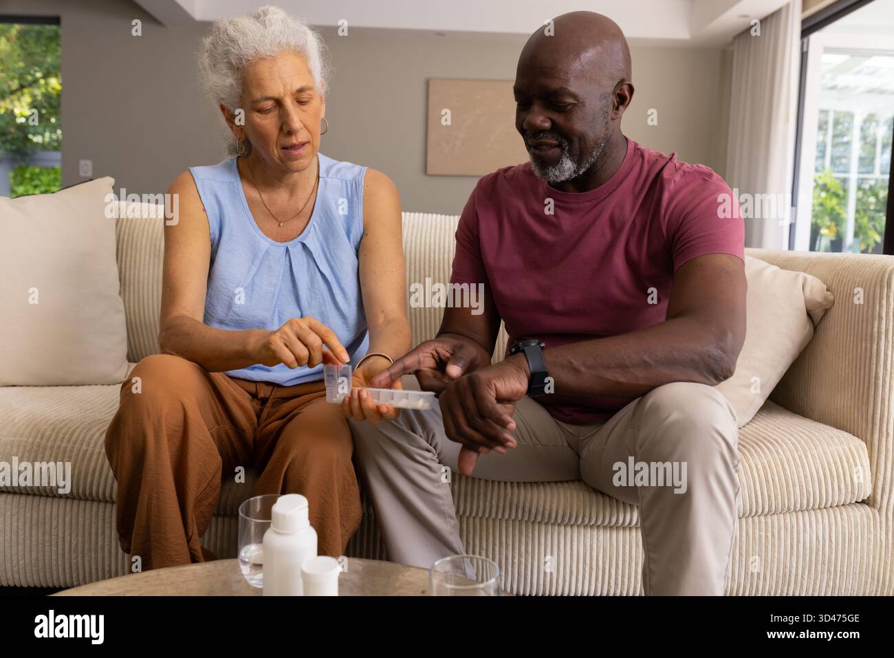 Diverse Seniorenpaare sortieren Pillen in wöchentlichen Pillen Organizer auf Sofa, mit verschreibungspflichtigen Flaschen Stockfoto
