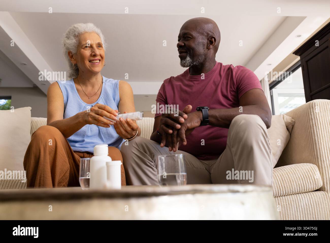 Sortieren verschiedener Seniorenpaare, die Pillen-Flaschen im Wohnzimmer verwalten, mit Pillen-Organizer Stockfoto