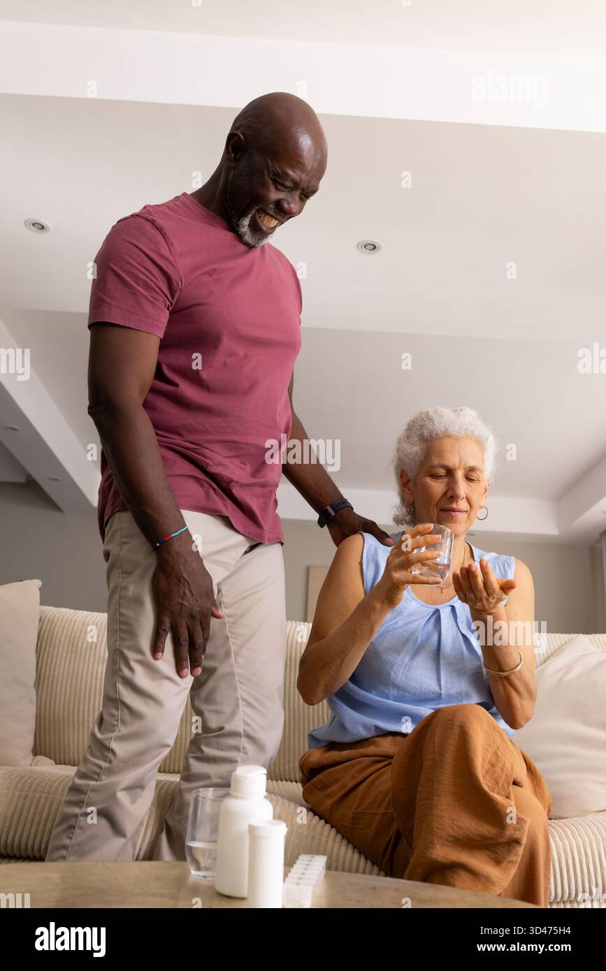 Diverse Seniorenpaare, die Medikamente im modernen Wohnzimmer mit Pillen-Organizer und Wasser vorbereiten Stockfoto