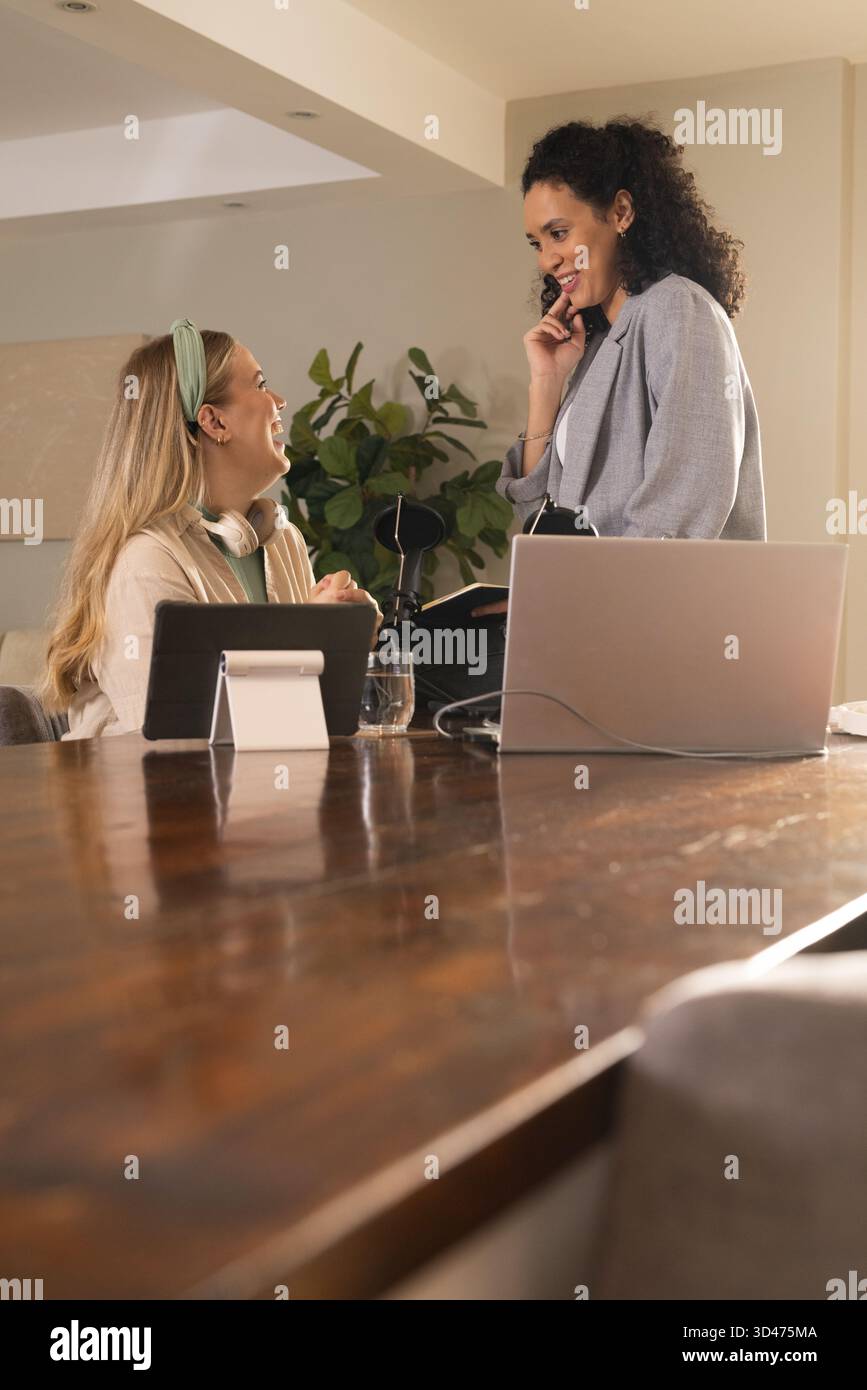 Zusammenarbeit mit verschiedenen weiblichen Kollegen, die am Tisch im Home Office arbeiten, mit Laptop und Mikrofon Stockfoto