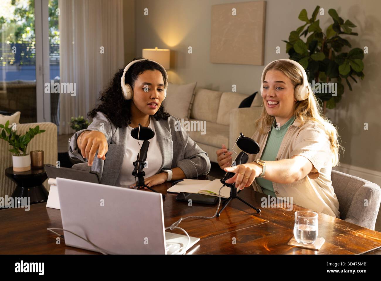 Aufnahme verschiedener weiblicher Kollegen, die Podcasts im Wohnzimmer halten, mit Laptop und Mikrofonen Stockfoto