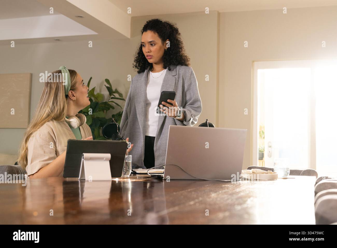 Verschiedene weibliche Kollegen arbeiten an einem Holztisch im Heimbüro zusammen, mit Laptop und Tablet Stockfoto