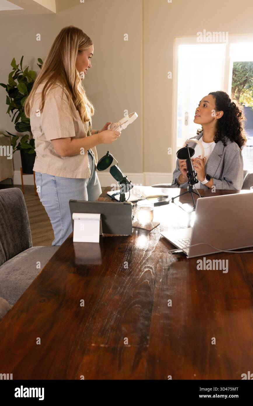 Verschiedene weibliche Kollegen arrangieren Audiogeräte am Schreibtisch im Heimbüro mit Mikrofonen Stockfoto