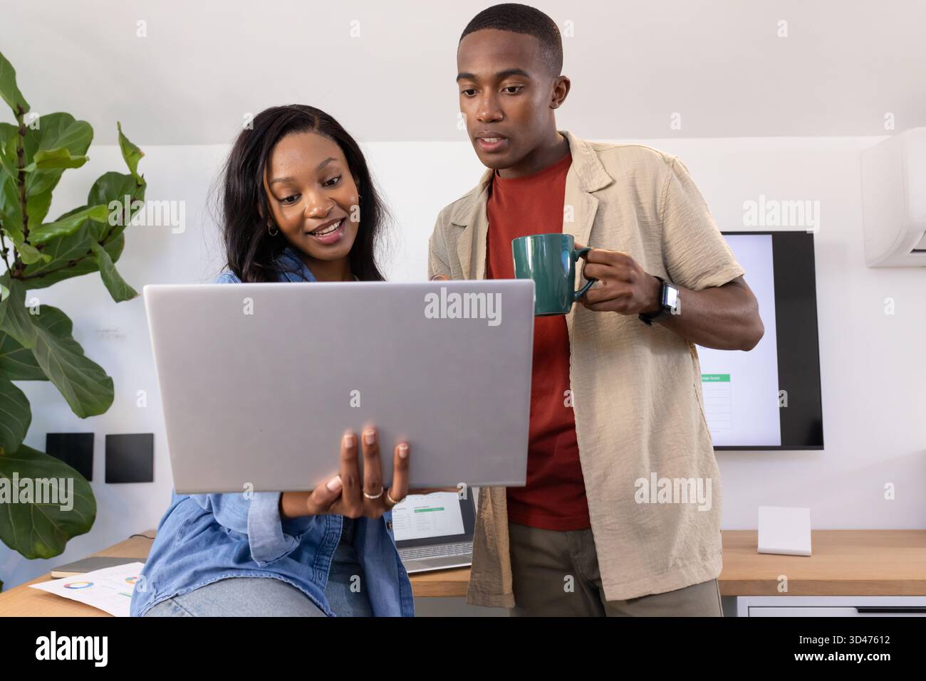 Kooperierende afroamerikanische Kollegen diskutieren Projekt im modernen Büro, mit Laptop und Becher Stockfoto