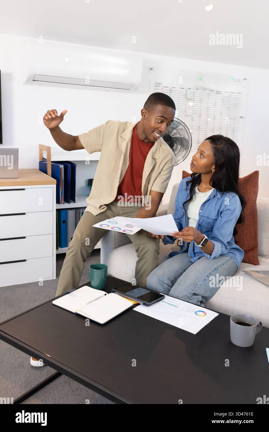 Afroamerikanische Kollegen untersuchen Karten auf der Couch im Heimbüro, mit Kaffeetassen Stockfoto