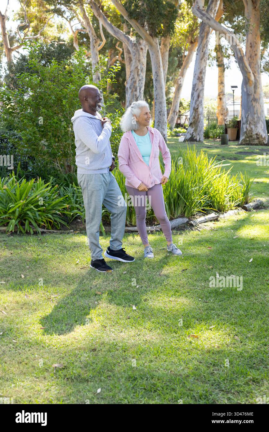 Sie unterhalten sich mit verschiedenen älteren Freunden, die sich auf dem grasbewachsenen Rasen im Park aufwärmen, und üben Outdoor-Übungen Stockfoto