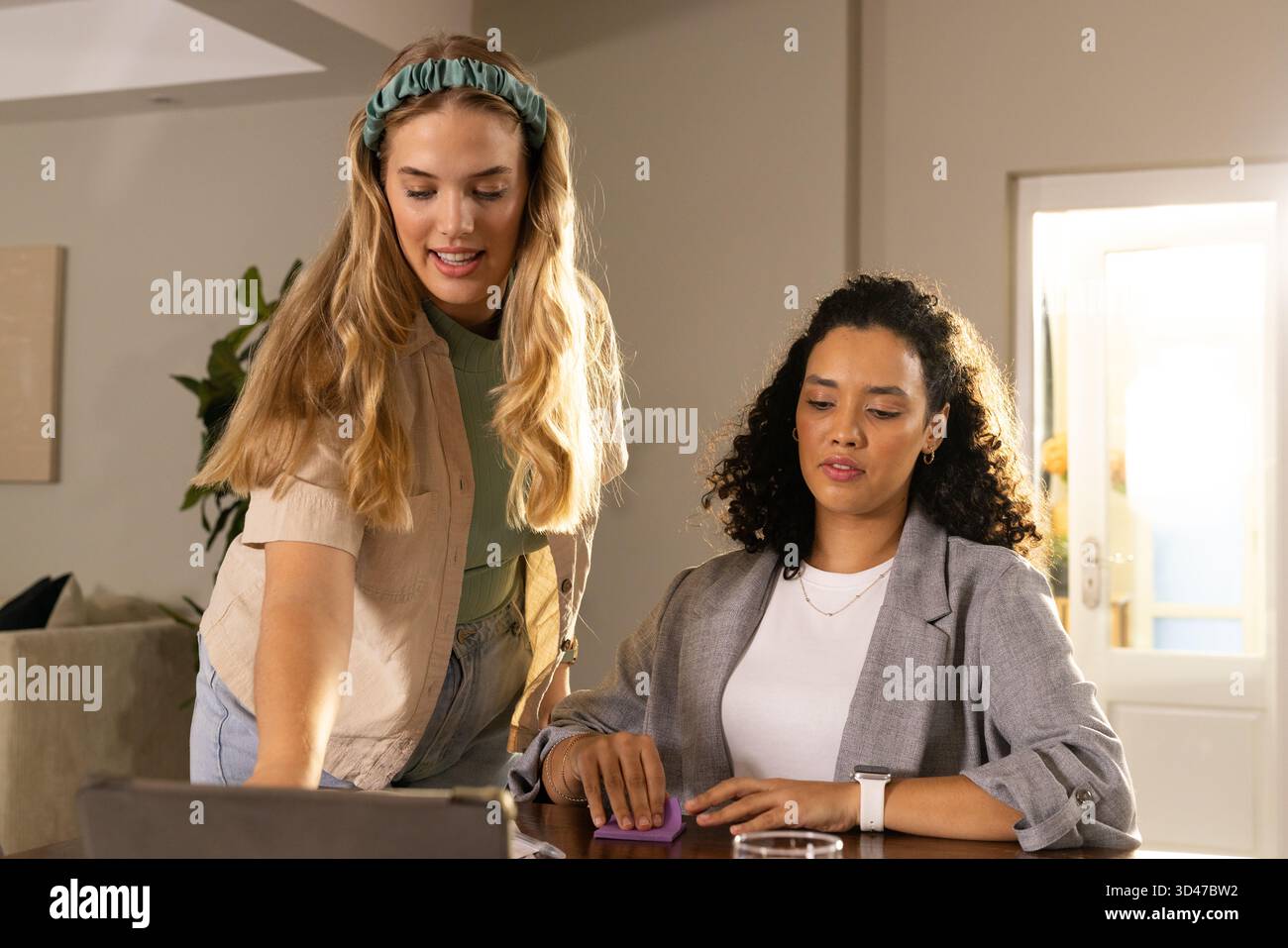 Kooperierende Freundinnen, die auf einen Laptop im Wohnzimmer zeigen, mit kabellosem Touchpad Stockfoto