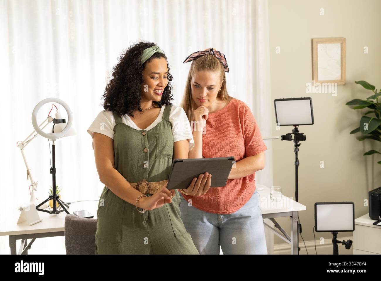 Zusammenarbeit mit verschiedenen weiblichen Freunden, die den Tablet-Bildschirm im Heimstudio mit Ringlicht untersuchen Stockfoto