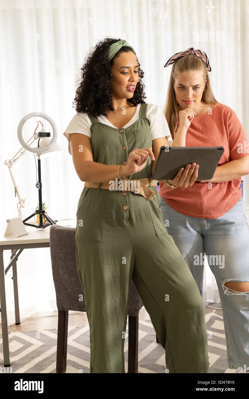 Diskutieren von Inhalten, verschiedene weibliche Freunde arbeiten im Heimstudio mit Tablet und LED-Ringlicht zusammen Stockfoto
