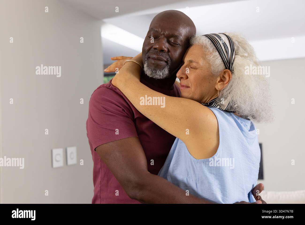 Ein vielseitiges Seniorenpaar, das sich sanft umarmt in einem modernen Wohnbereich mit sanfter Beleuchtung Stockfoto