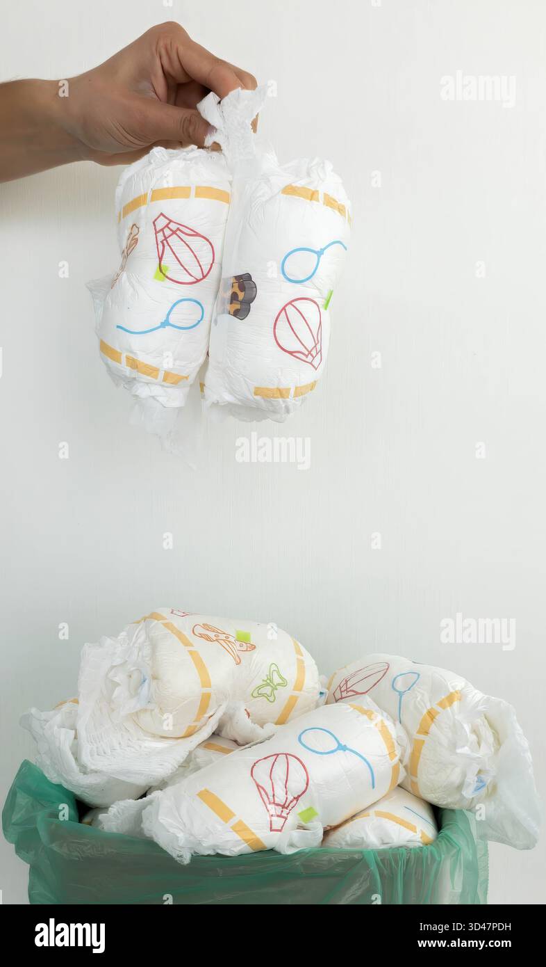 Die Hand wirft gebrauchte Windeln in den vollen Papierkorb. Stockfoto